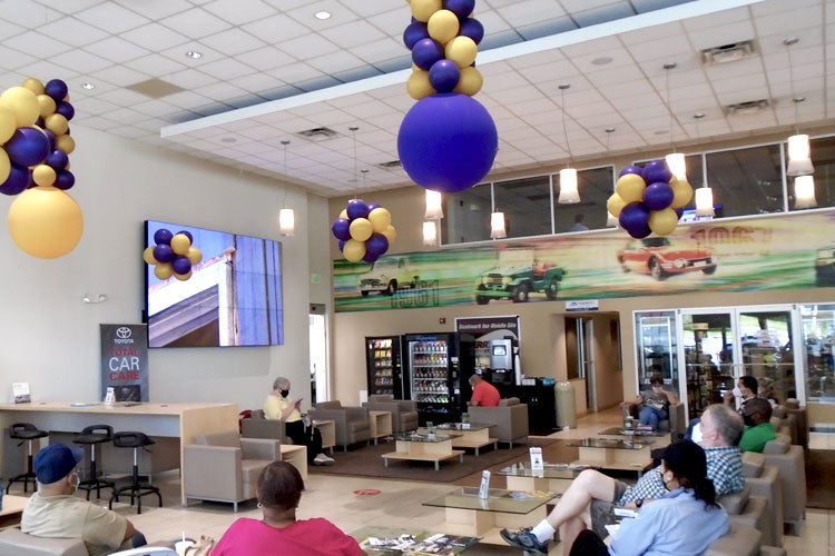 People sitting on a couch in the service waiting area watch giant screen